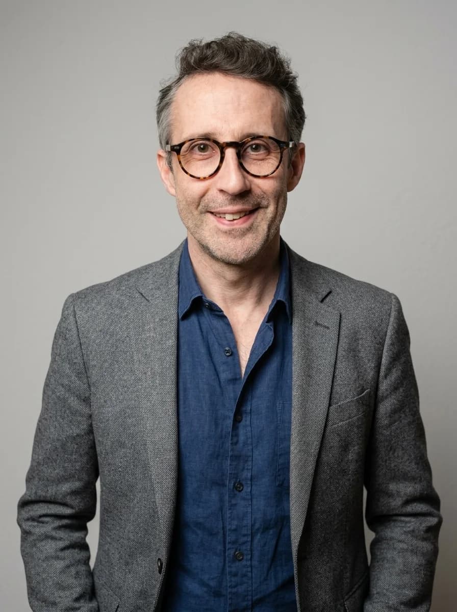 Portrait IA dentiste style corporate chaleureux — blazer gris chiné et chemise denim, sourire franc, lumière studio douce et tons chair naturels